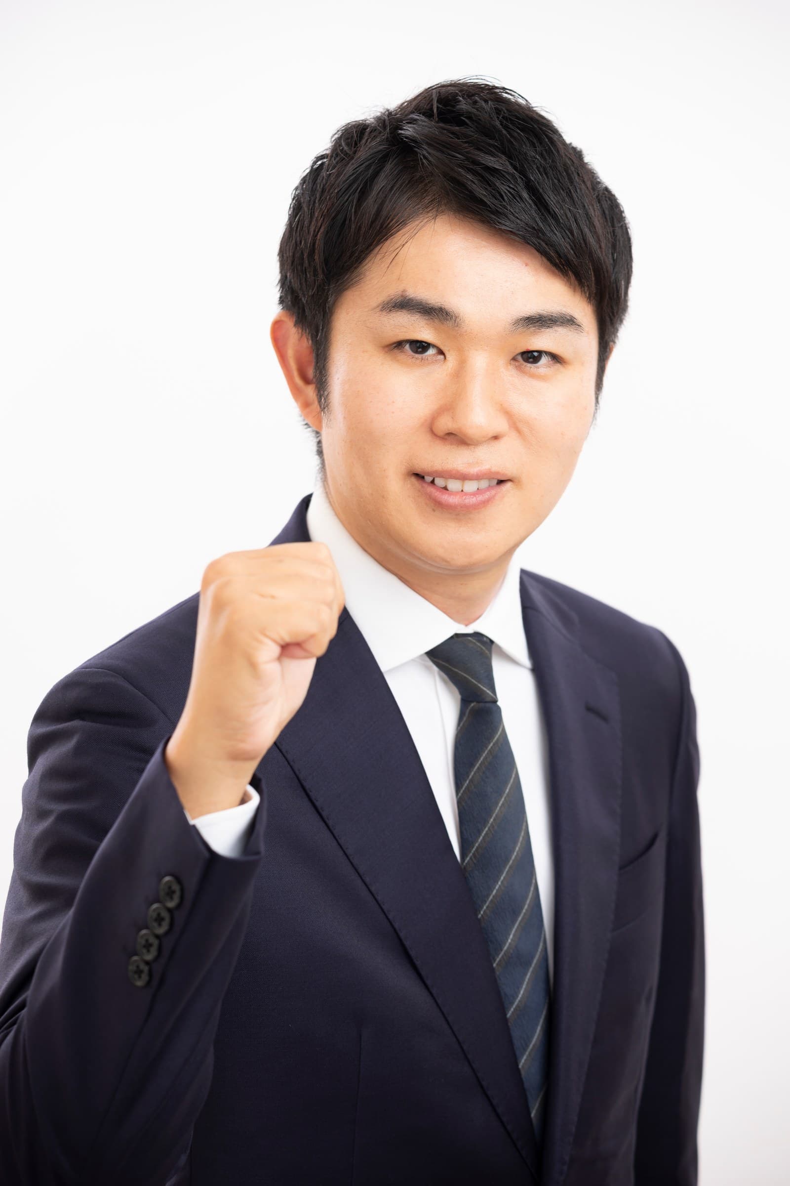スーツ姿で笑顔を見せ、右手の拳を掲げる菊川 道一